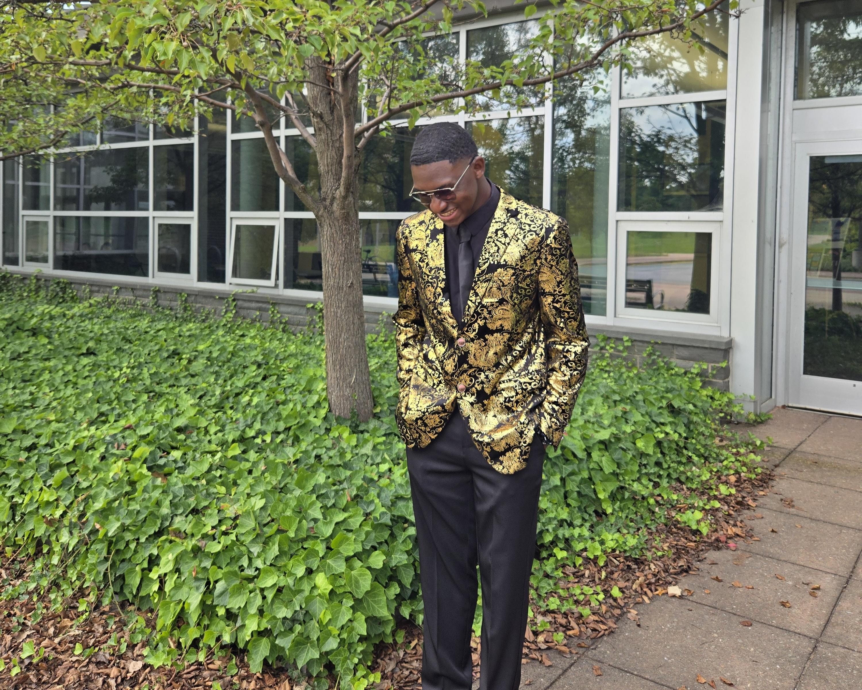 Oswego student Jamal Akin-Tukur stands outside Marano Campus Center wearing a gold blazer and black dress pants.