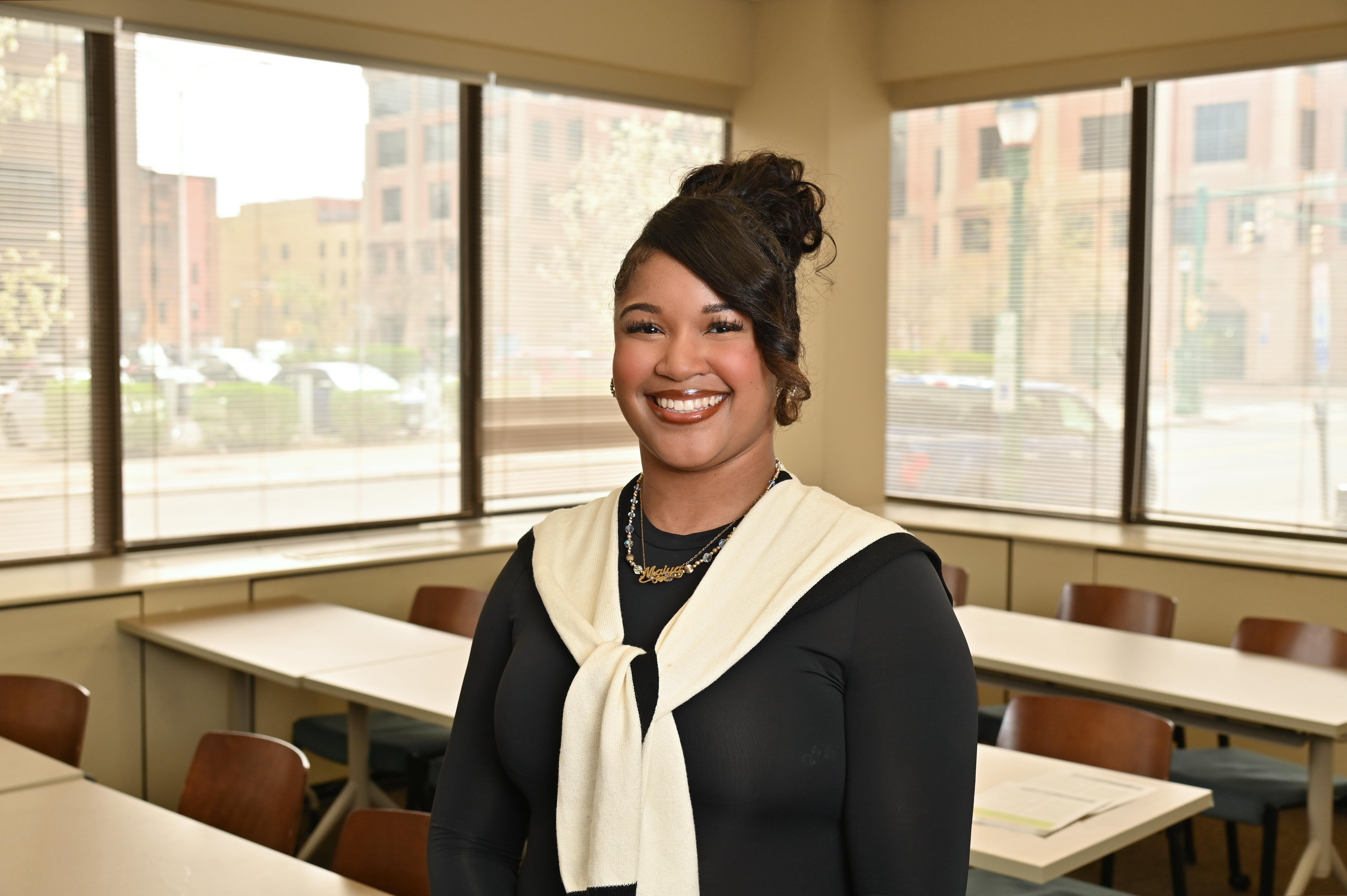Maiya White smiles in a classroom at SUNY Oswego at Syracuse, where she completed her degree while balancing teaching, parenting and coursework.