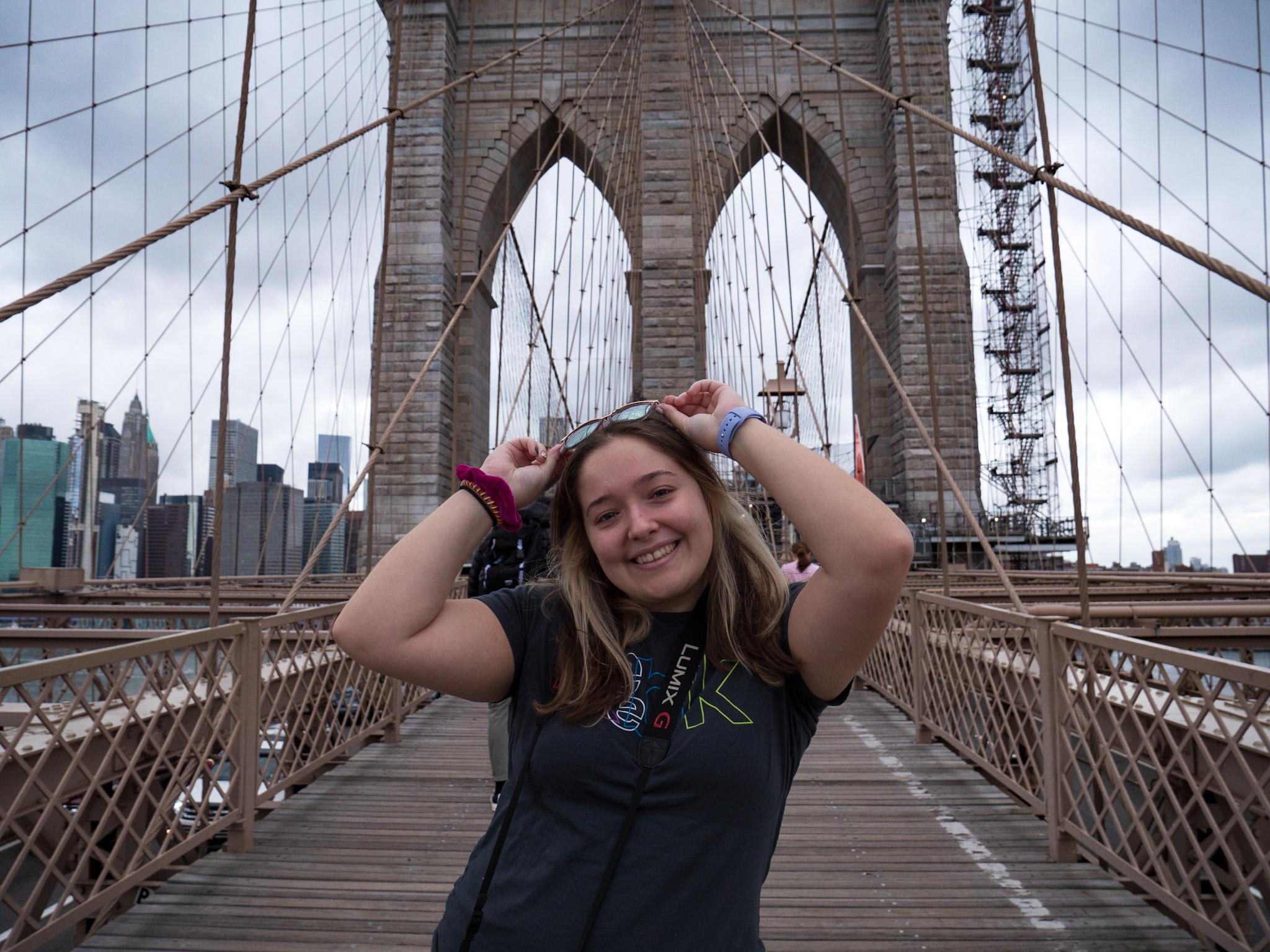 Alum Corey Cesare on the Brooklyn Bridge. Alum Corey Cesare smiling with a camera on the Brooklyn Bridge.