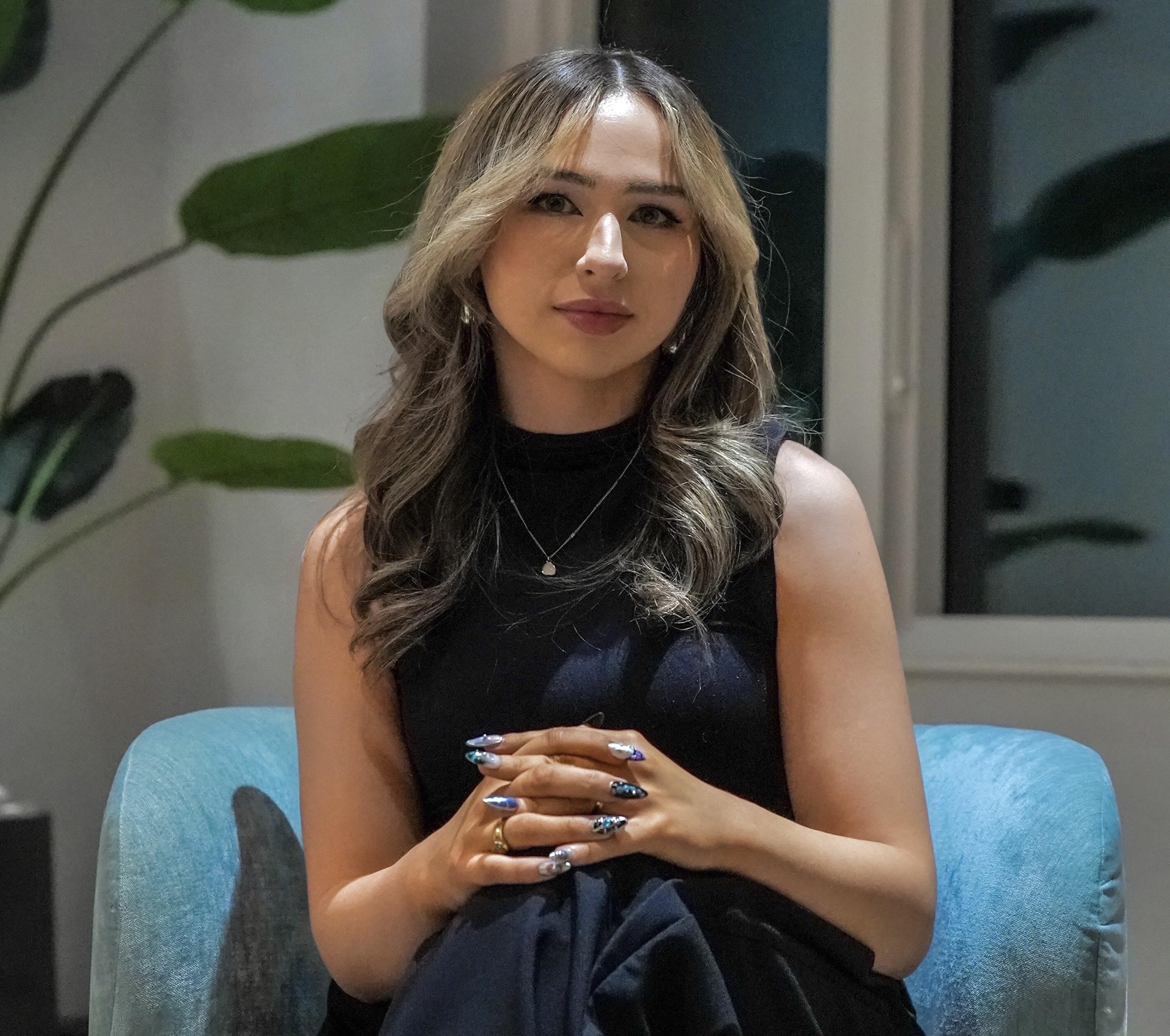 SUNY Oswego alumna Samantha Brown seated in a teal chair, wearing a black sleeveless outfit, posing for a professional portrait indoors.