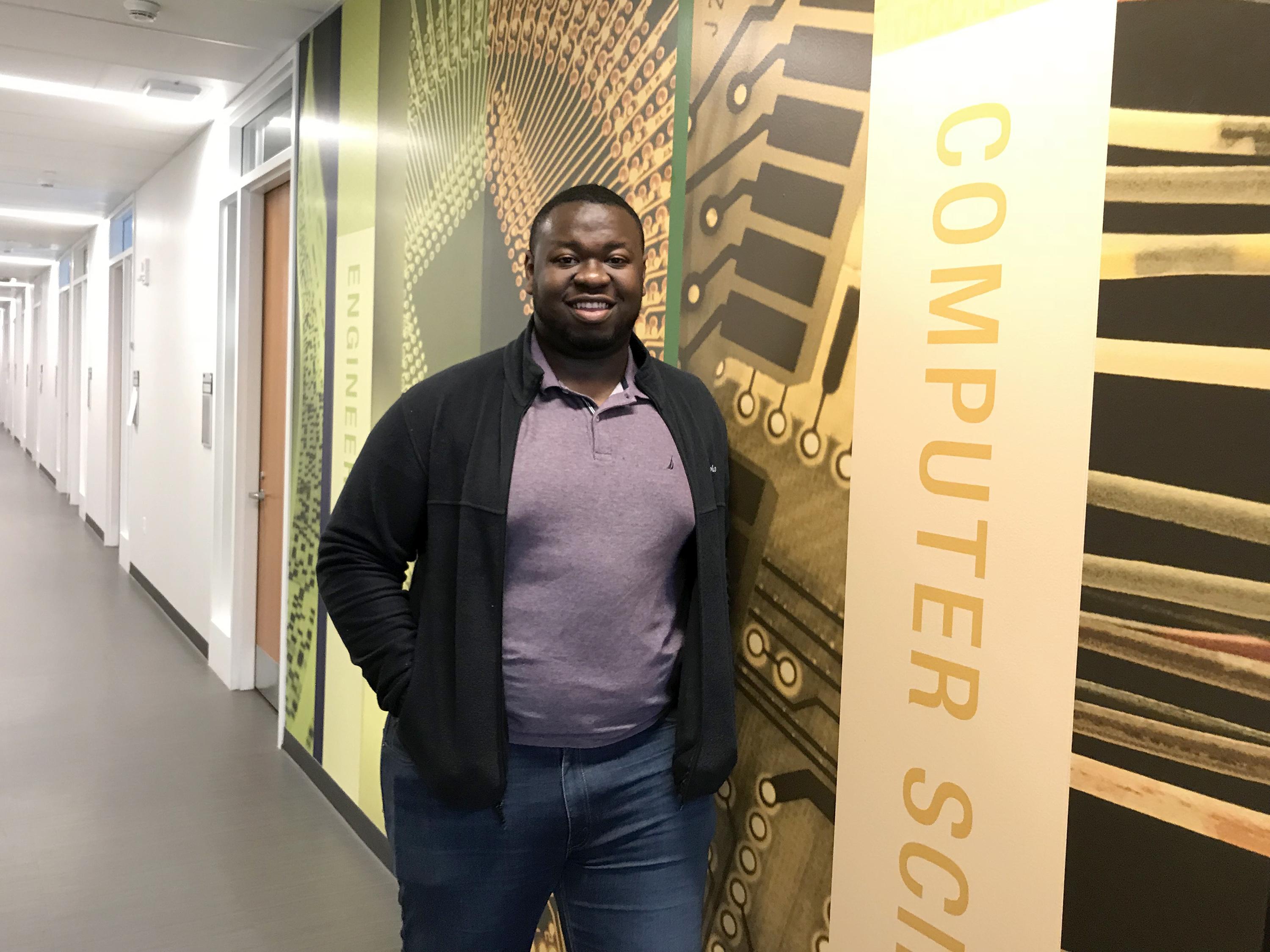 Kingsley Ibezim in front of a mural on computer science and other fields in the Shineman Center