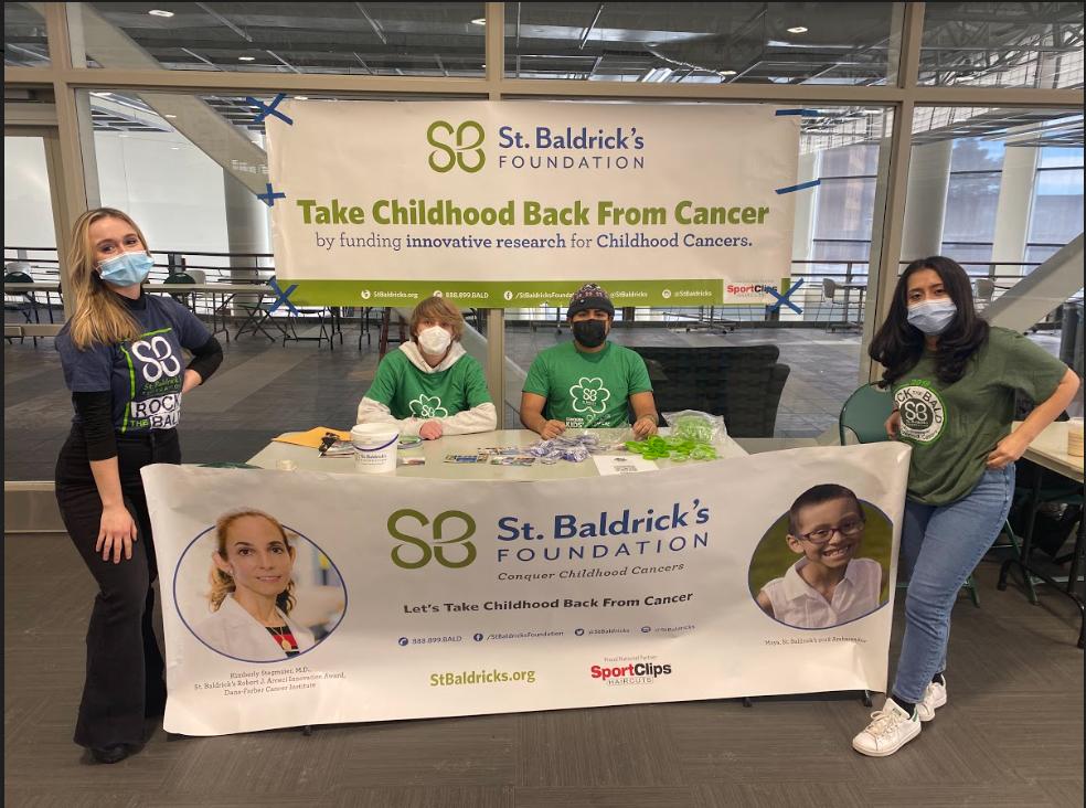 Group of four students work a table with St. Baldrick's banners to support the children's cancer charity