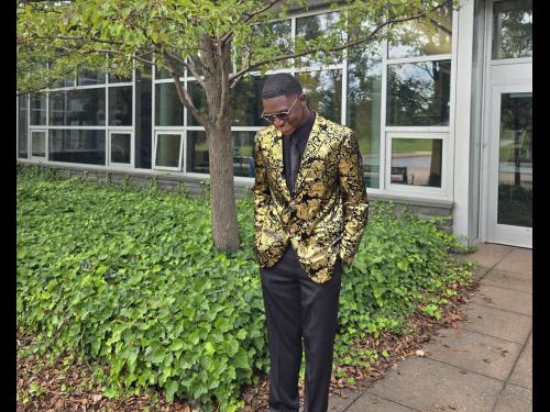 Oswego student Jamal Akin-Tukur stands outside Marano Campus Center wearing a gold blazer and black dress pants.