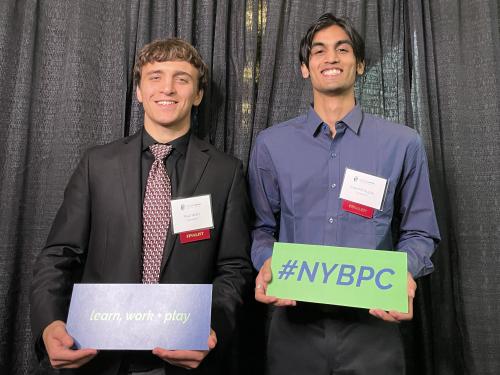 SUNY Oswego students Paul Wehr and Harshit Gupta at the New York State Business Plan Competition, wearing red "finalist" badges.