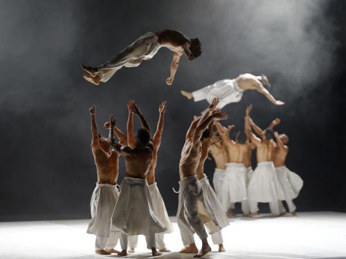 Dancers soar in the air as groups of fellow troupe member wait to catch them