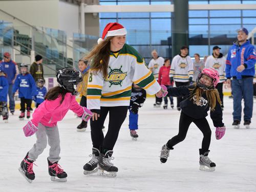 Two little girls skate with a women's hockey player