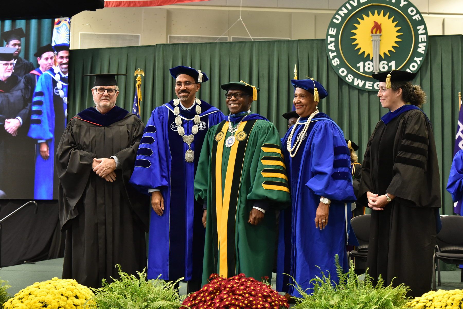 Members of the platform party presented SUNY Oswego’s 11th President Peter O. Nwosu (center) with the ceremonial hood and medallion during the Sept. 27 inauguration in the Deborah F. Stanley Arena and Convocation Hall.