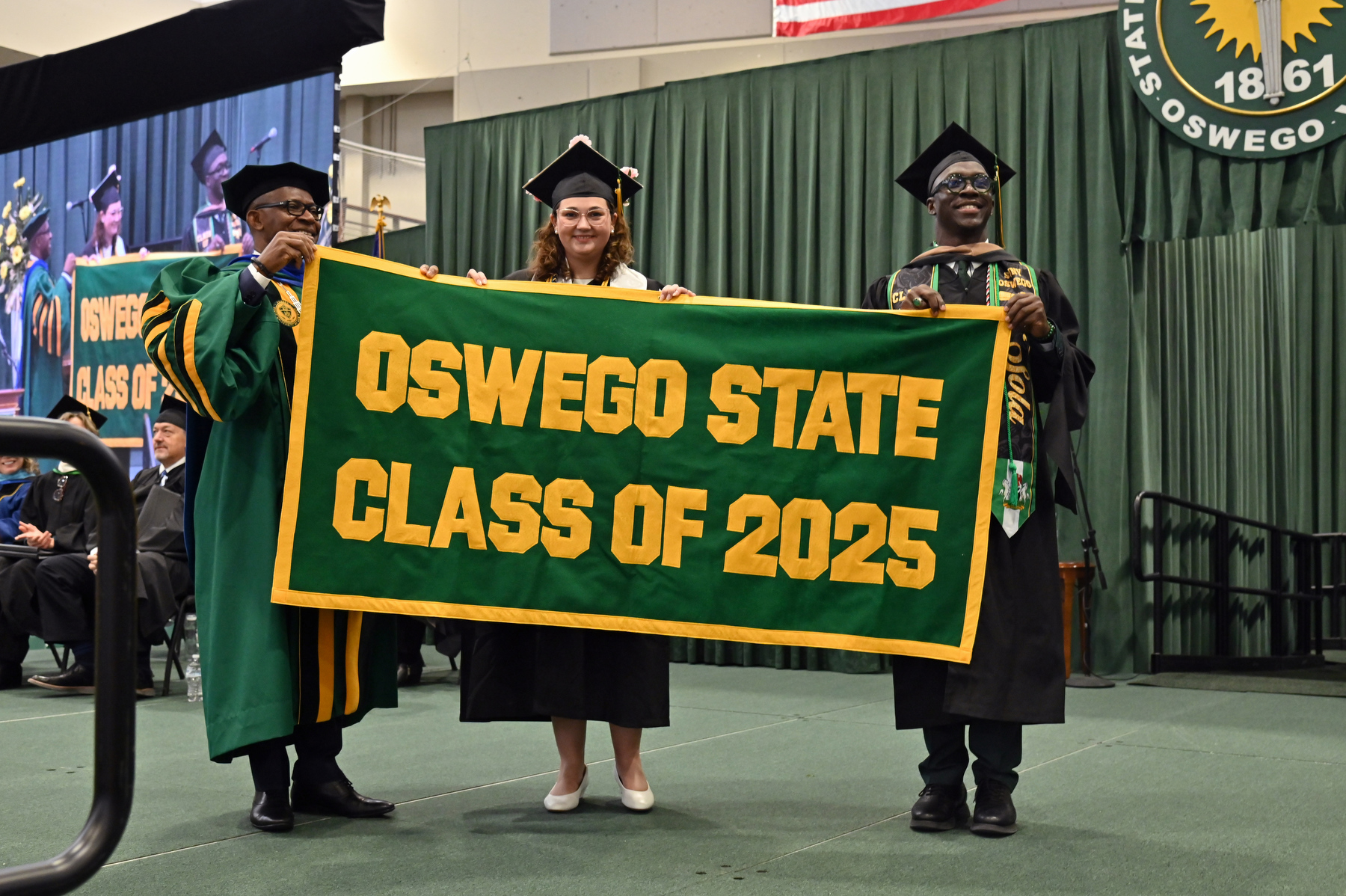 December Commencement celebrated graduates and their many supporters on Dec. 13 in the Deborah F. Stanley Arena and Convocation Hall, Marano Campus Center. President Peter O. Nwosu accepts the Class of 2025 Alumni Banner from undergraduate banner presenter Madison Flood and graduate banner presenter Olusola Fawehinmi.