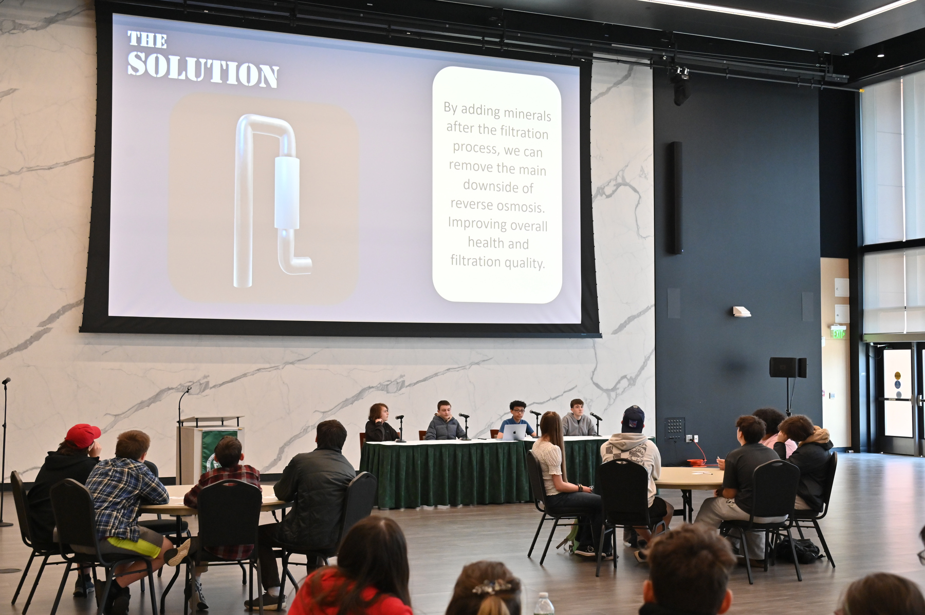 As part of SUNY Oswego’s Engineering Week with sponsorship from Micron Technology, students from the Oswego County CiTi BOCES Pathways in Technology Early College High School (P-TECH) program presented their engineering solutions and problem-solving skills in an Innovators Showcase April 10 in the Hewitt Hall Ballroom. Shown are the winning team, Project Orion, discussing their solution to water purification.
